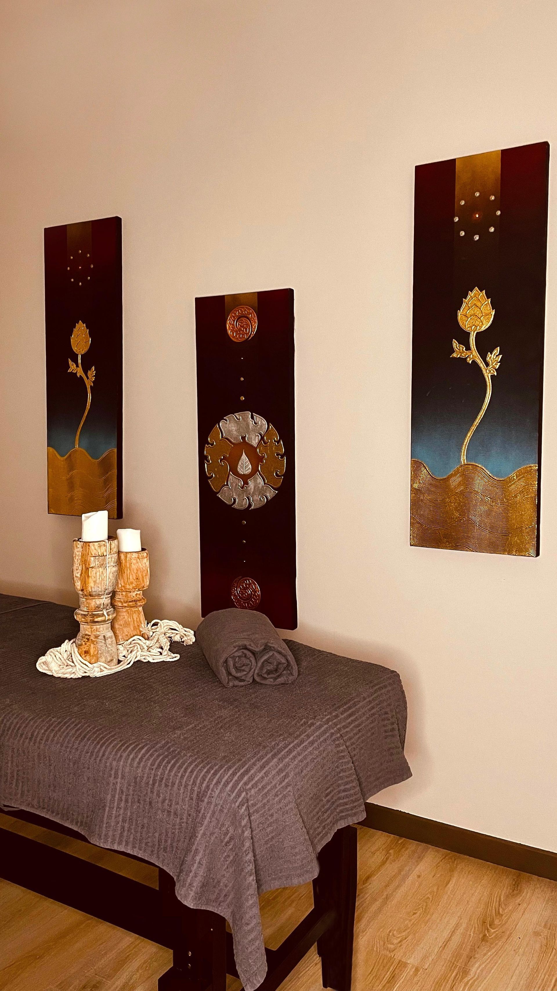 Un lettino per massaggi in una stanza con tre quadri alle pareti.