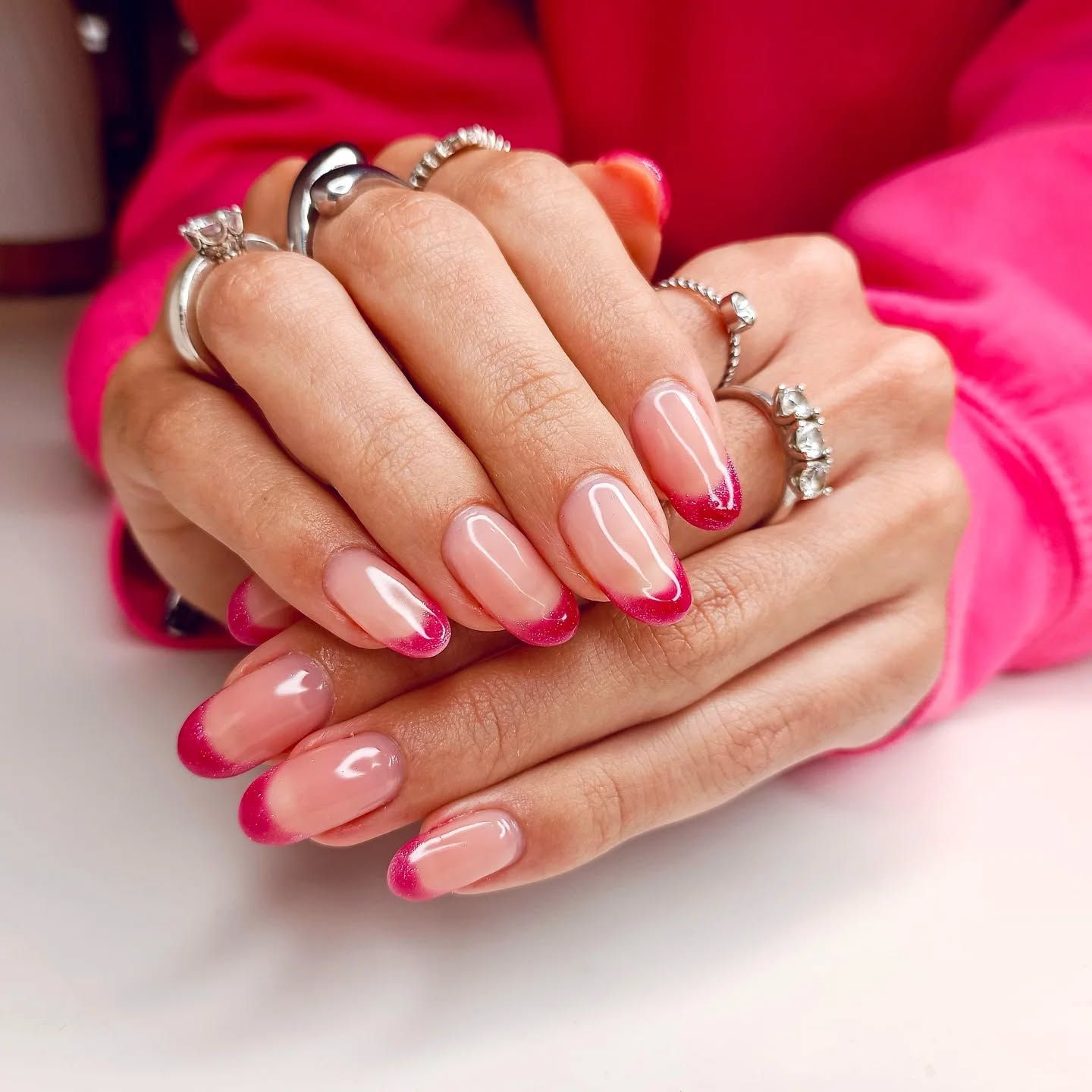 Un primo piano delle mani di una donna con unghie e anelli rosa.