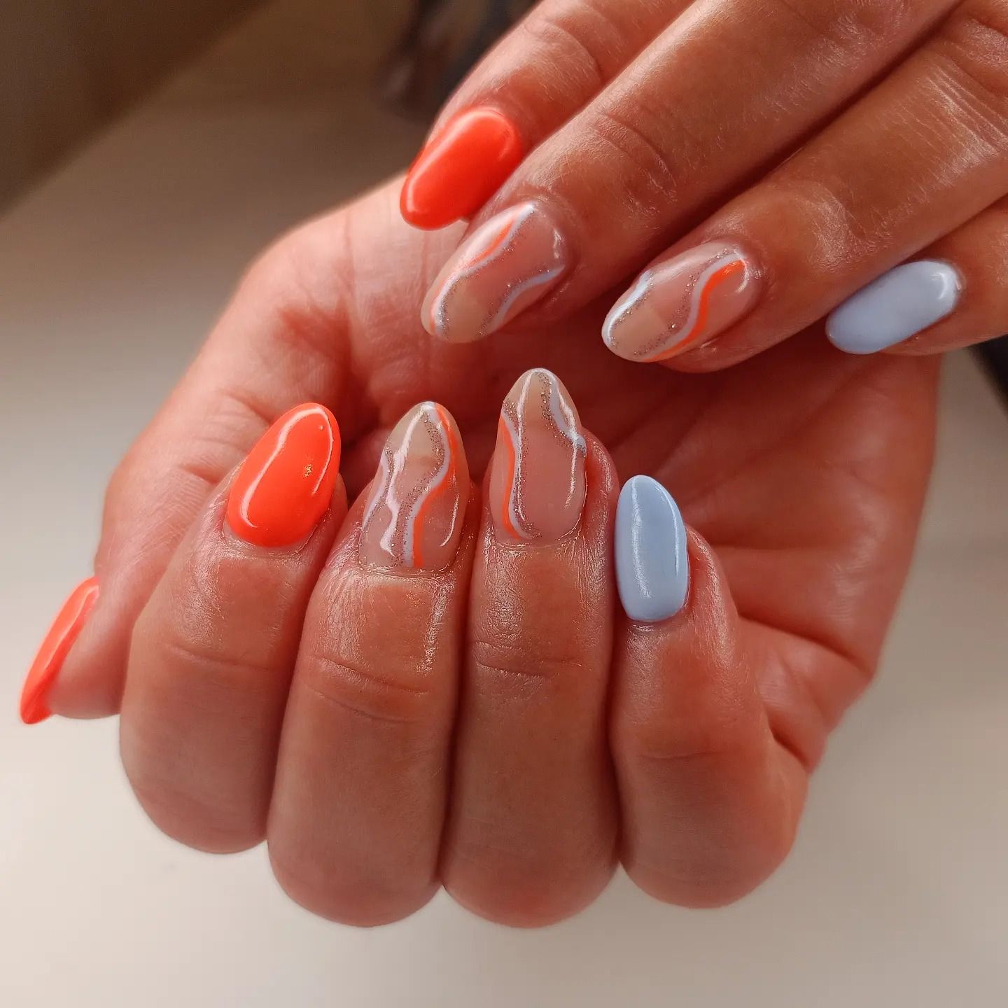 Un primo piano delle mani di una donna con unghie arancioni e blu