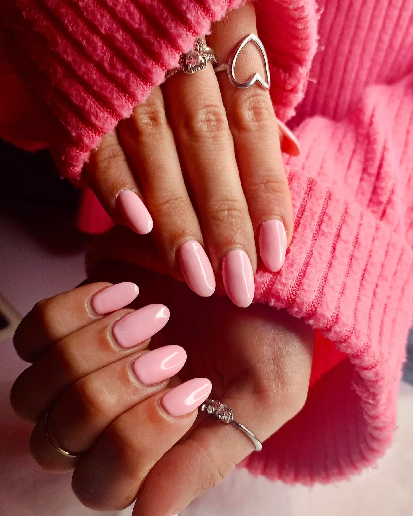 Una donna che indossa un maglione rosa ha unghie e anelli rosa alle dita