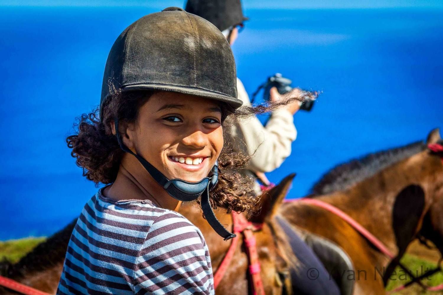 A young girl wearing a helmet is smiling while riding a horse.