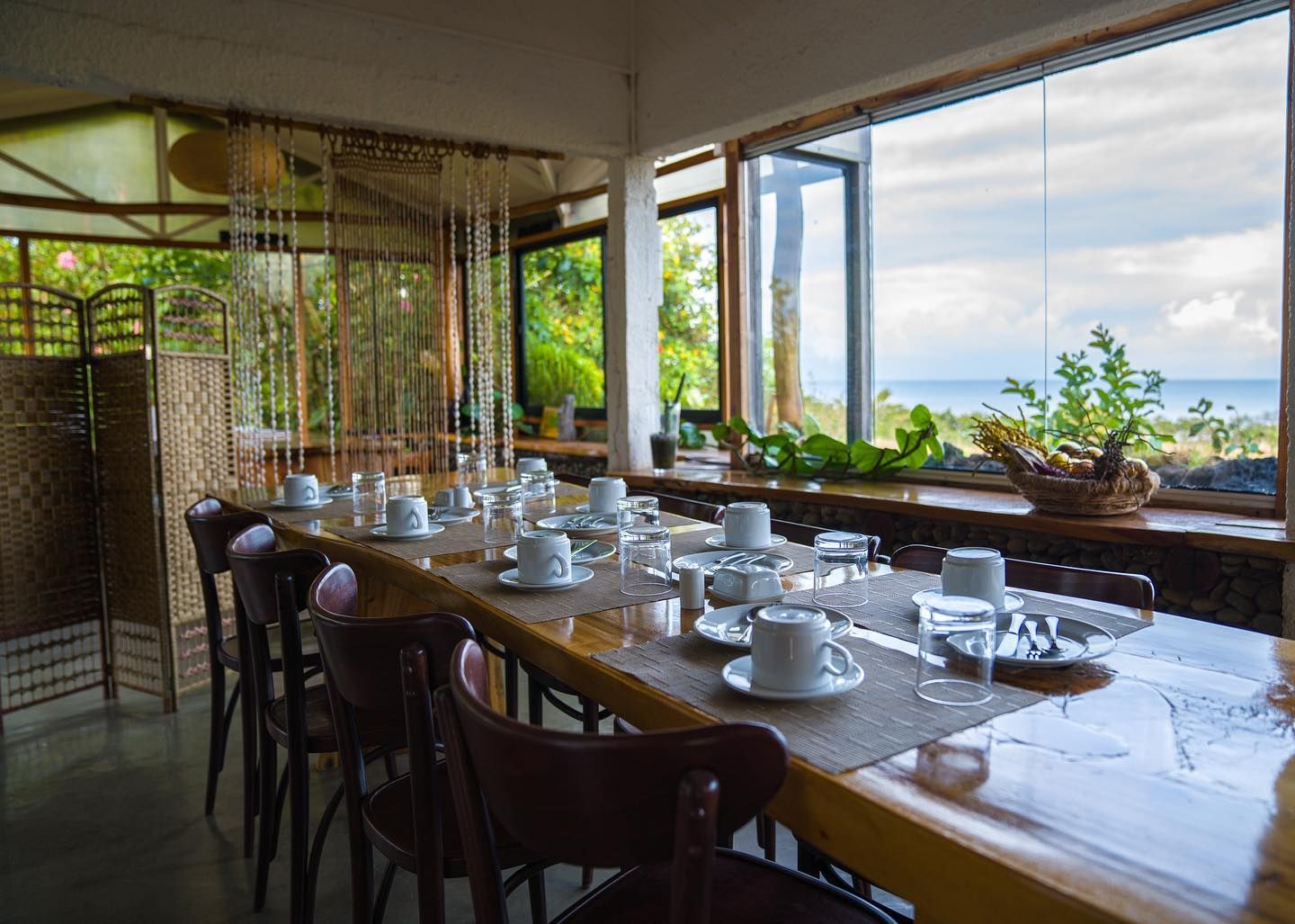 A restaurant with a long table and chairs and a view of the ocean.