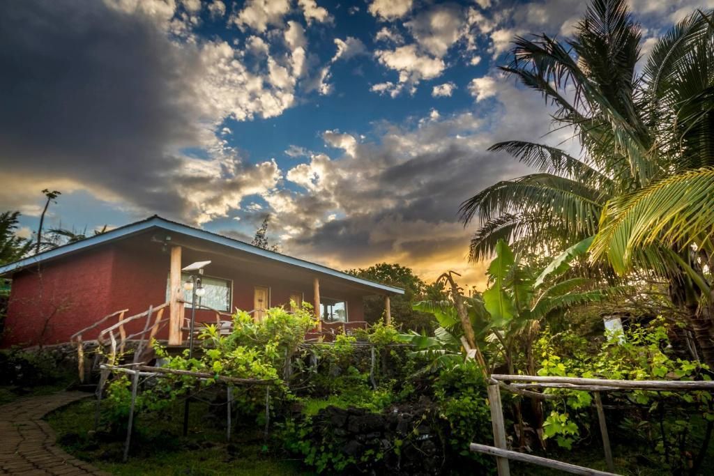 A red house is surrounded by palm trees and a fence.