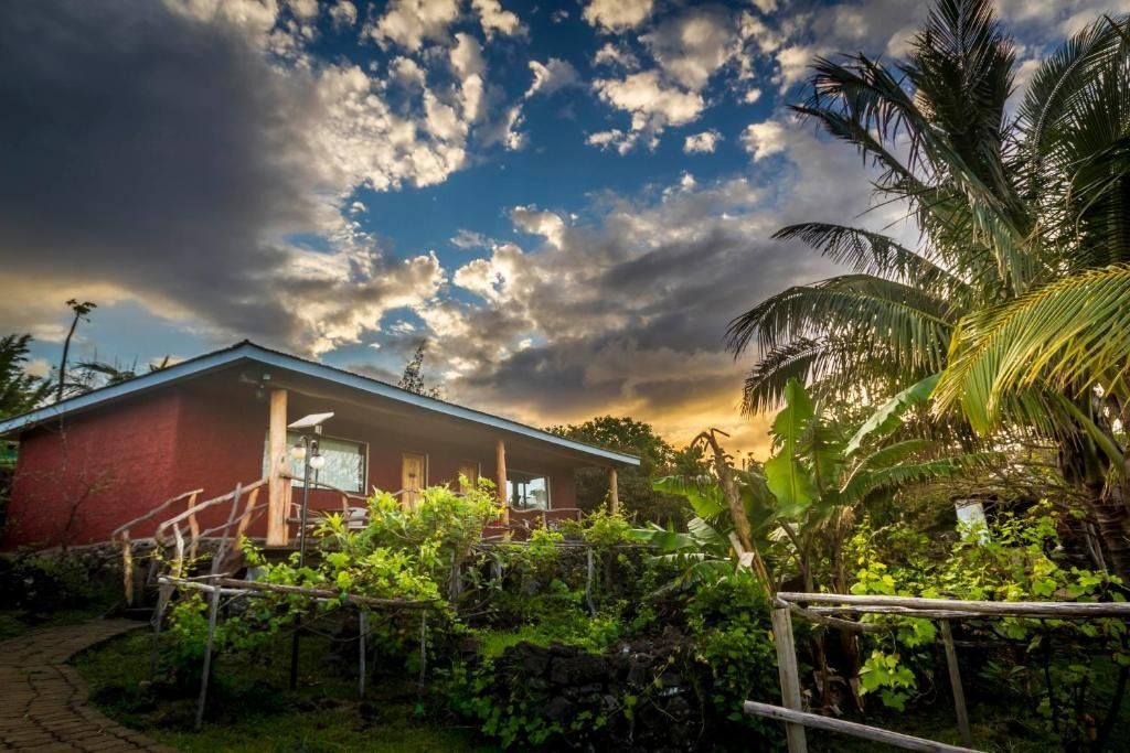 A red house is surrounded by trees and bushes under a cloudy sky.