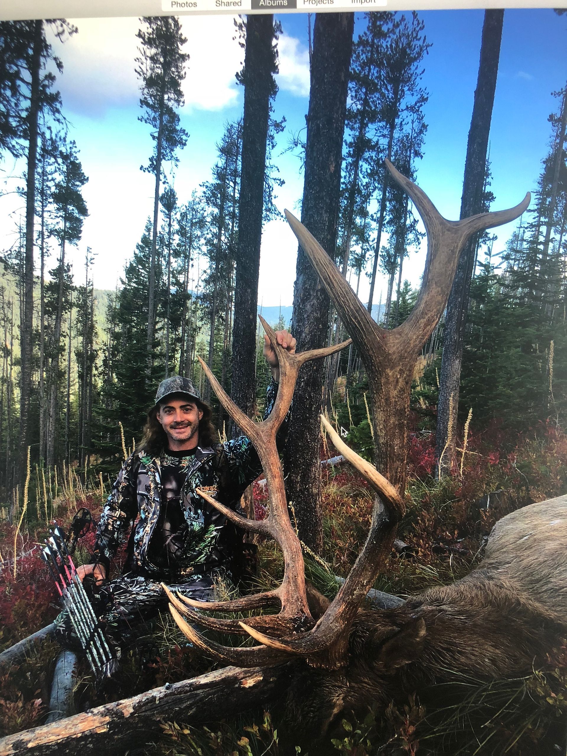 A man is standing in the woods holding a large deer antlers