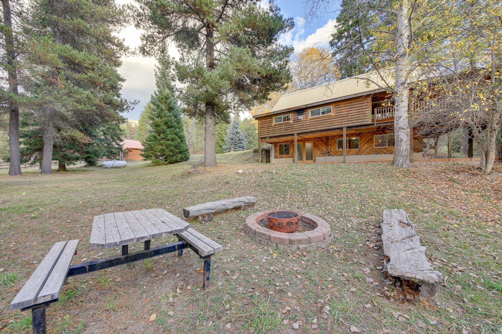 There is a picnic table and a fire pit in front of a log cabin.