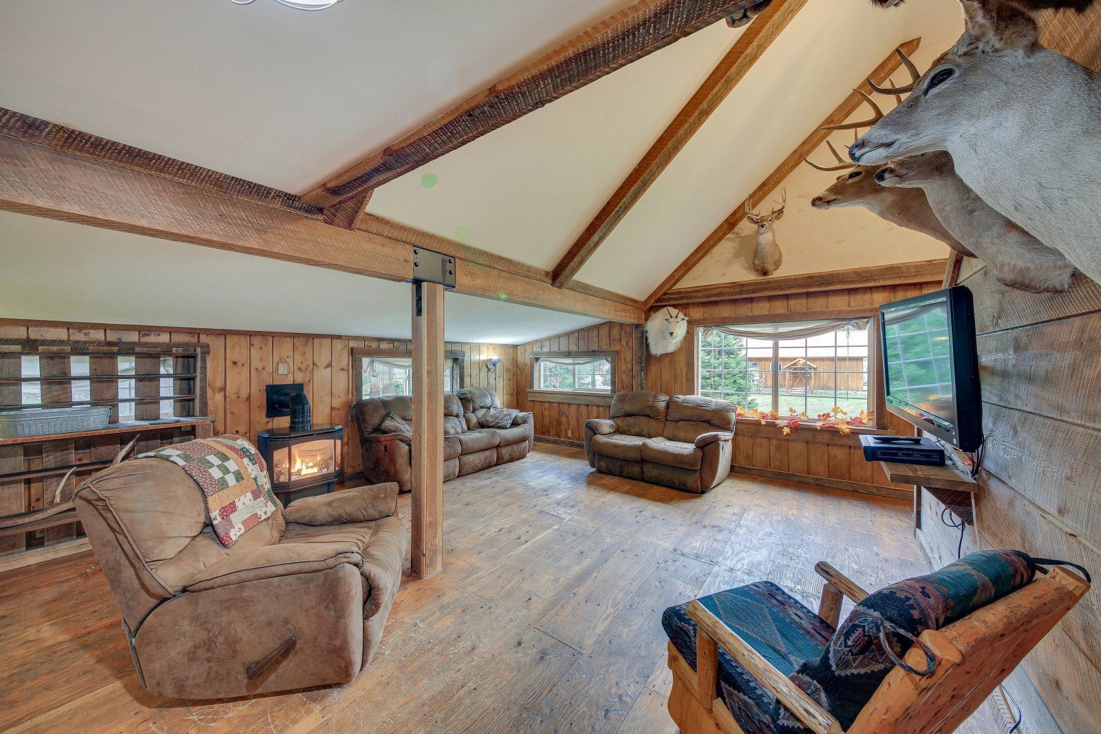 A living room with a couch , chairs , and a deer head on the wall.