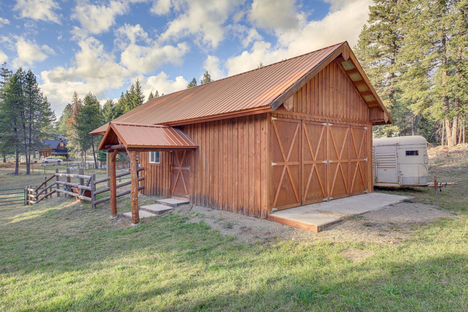 A wooden barn with a metal roof is sitting in the middle of a grassy field.