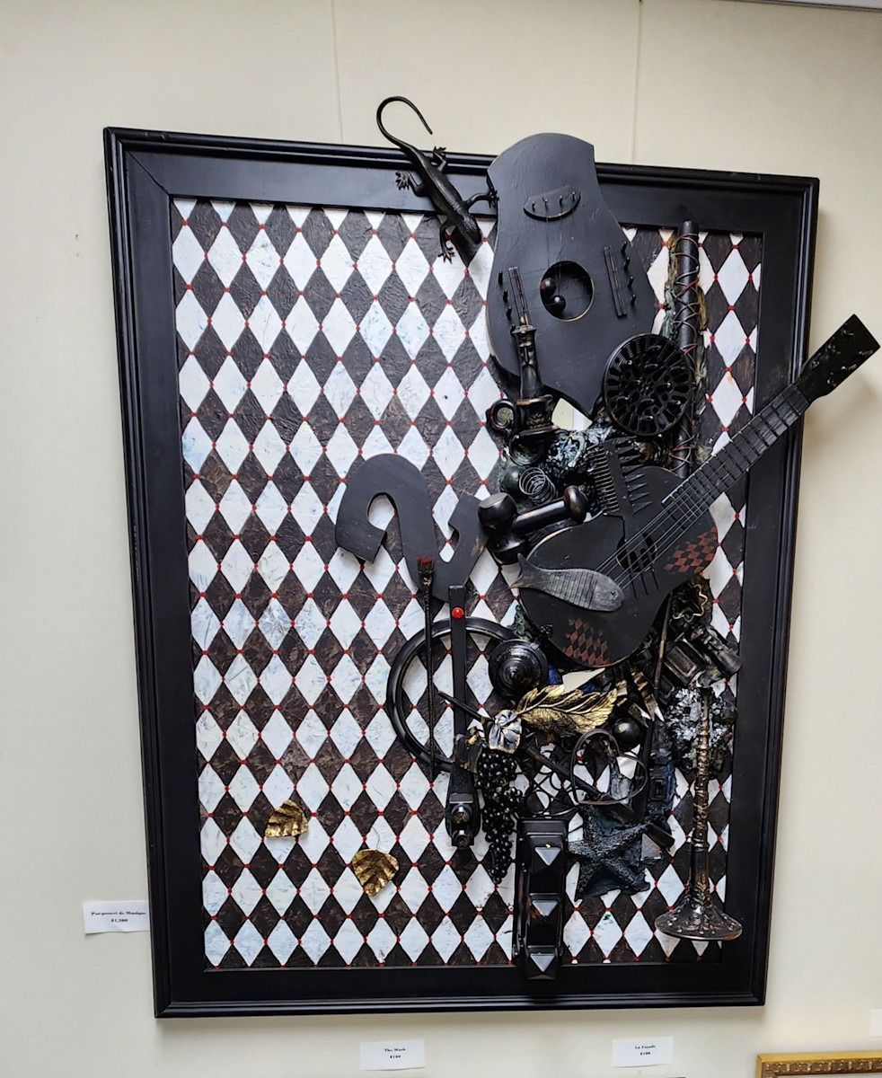 Black framed art with a checkered background. Black objects, including a guitar, are mounted on the surface.