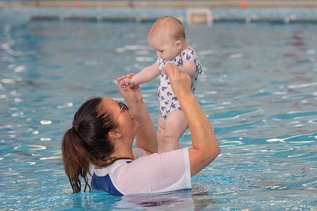 A woman is holding a baby in a swimming pool.