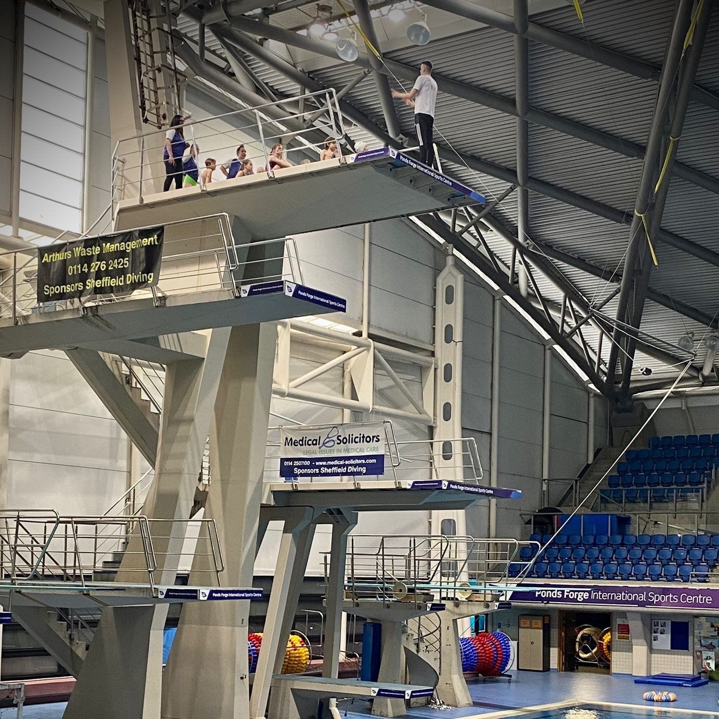A man is standing on top of a diving board in a swimming pool.