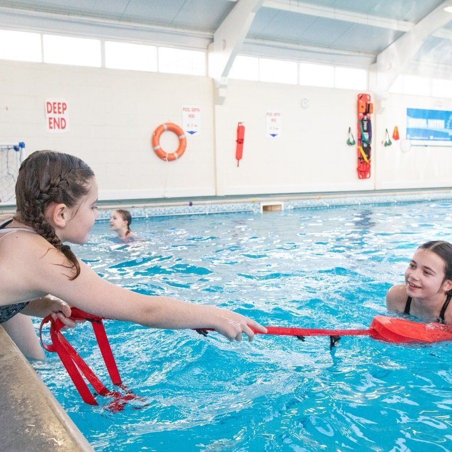 Two young girls are playing in a swimming pool with a life preserver.