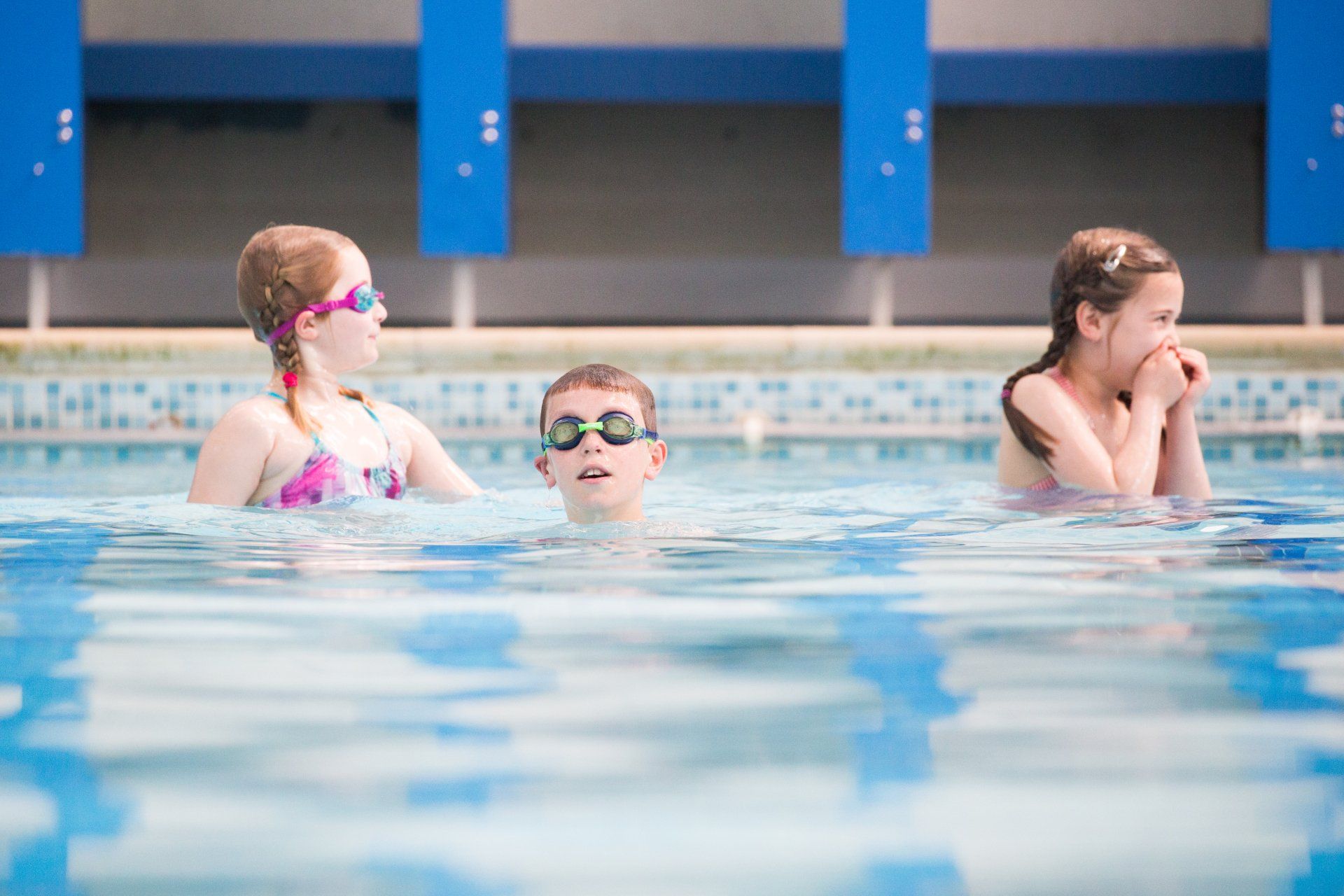 A boy and two girls are swimming in a swimming pool.