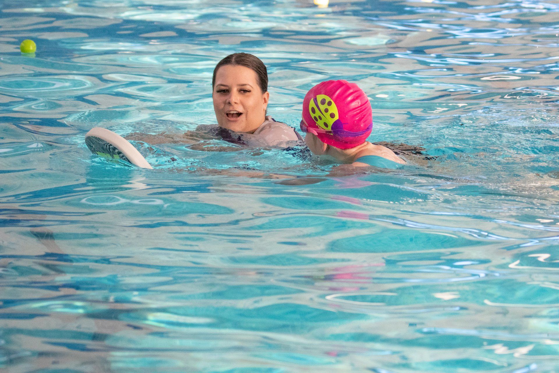 A woman is teaching a child how to swim in a swimming pool.