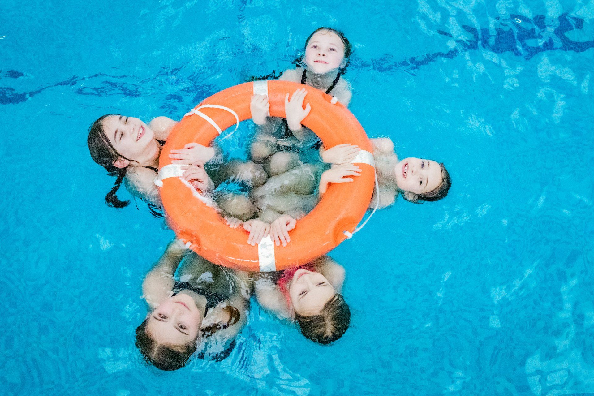 A group of children are swimming in a pool holding a life preserver.