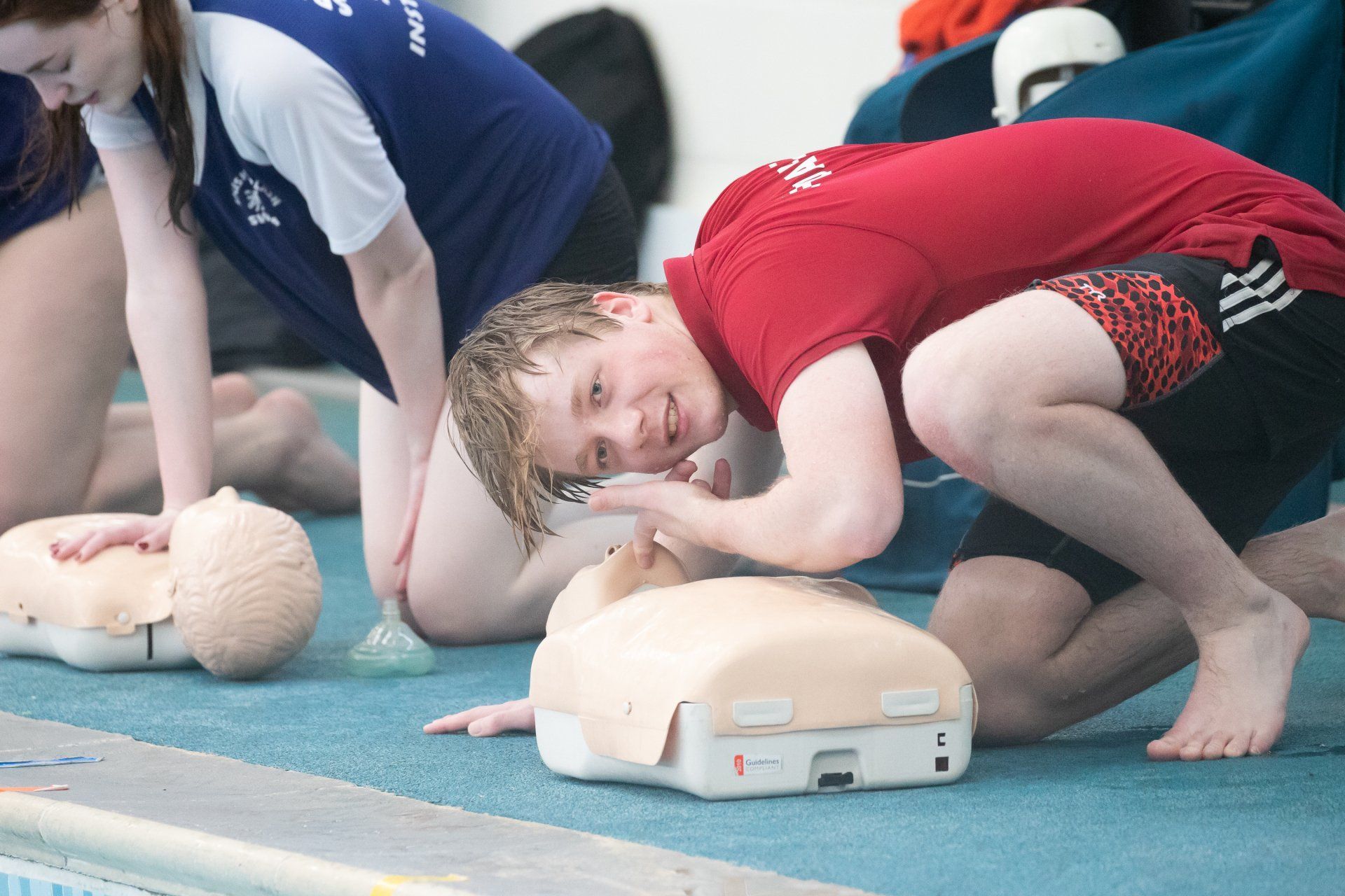 A man in a red shirt is doing a cpr on a mannequin.