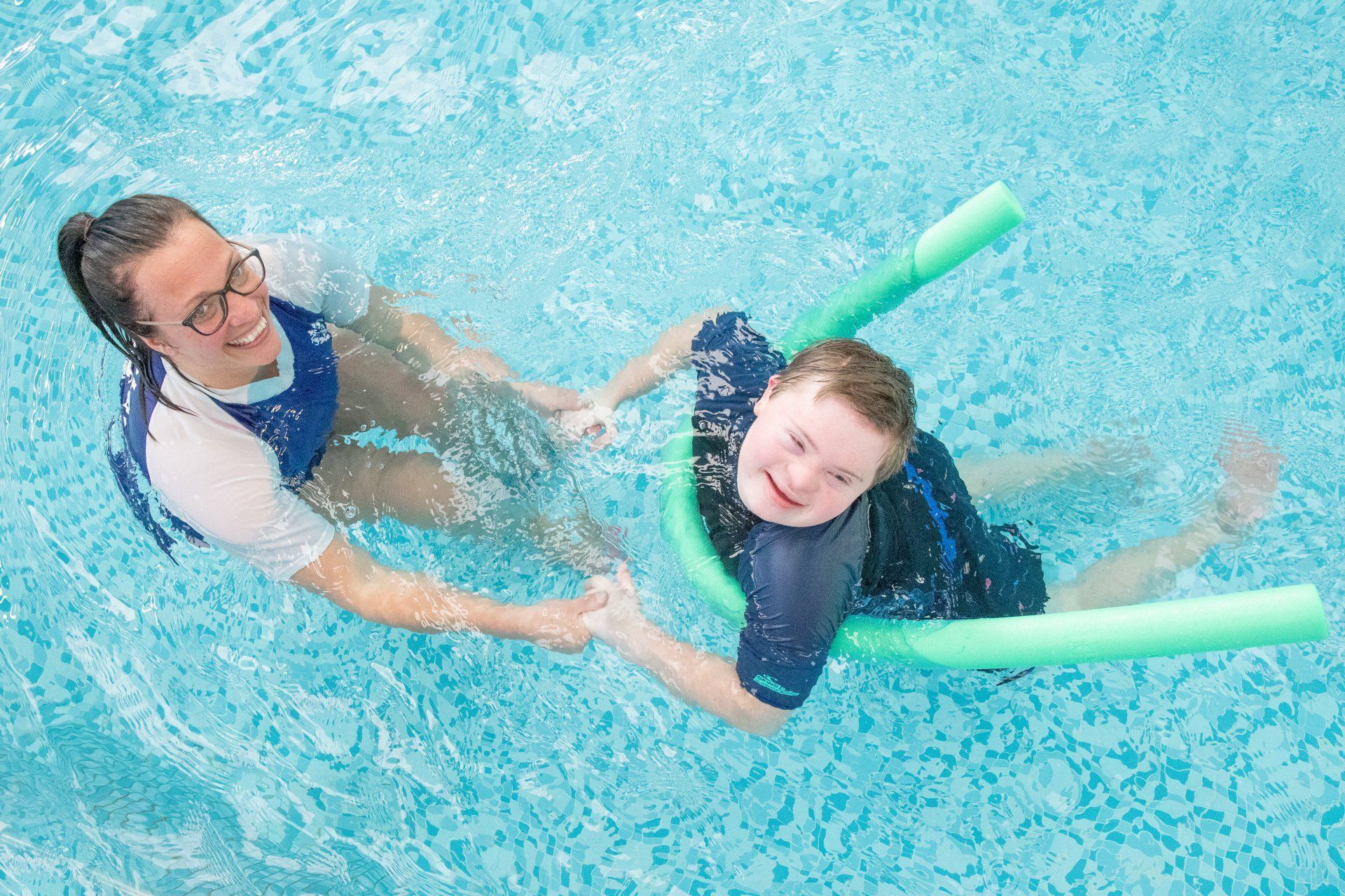 A woman is teaching a boy how to swim in a swimming pool.
