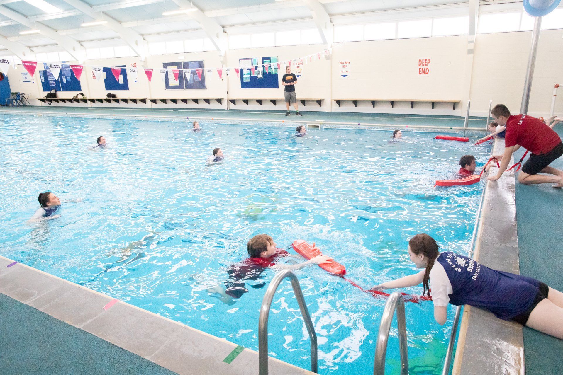 A group of people are swimming in a large indoor swimming pool.