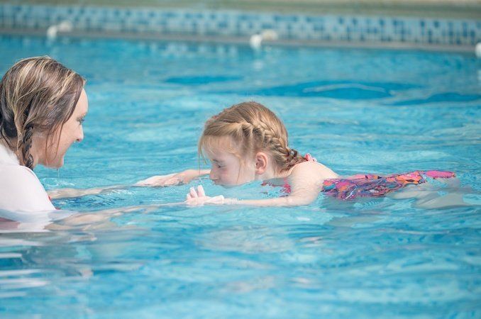A woman is teaching a little girl how to swim in a swimming pool.