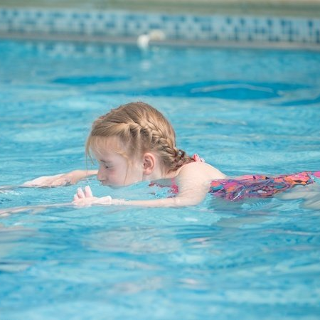 A little girl is swimming in a swimming pool.