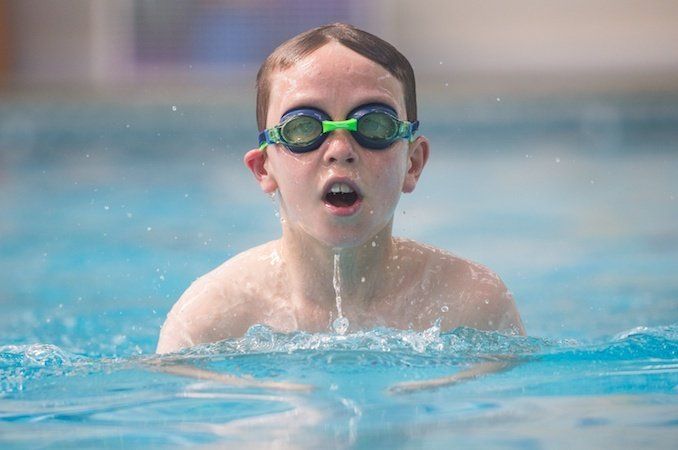A young boy wearing goggles is swimming in a swimming pool.