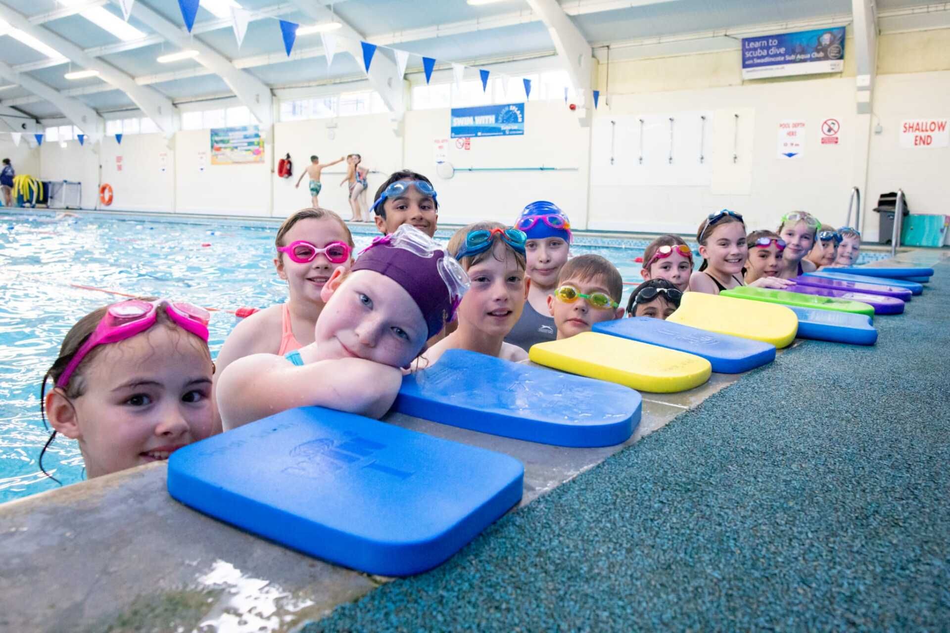 A group of children are standing on the edge of a swimming pool.