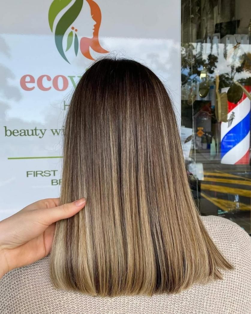 A Person Is Holding a Woman's Hair in Front of A Sign — Eco Village Hair in Bongaree, QLD