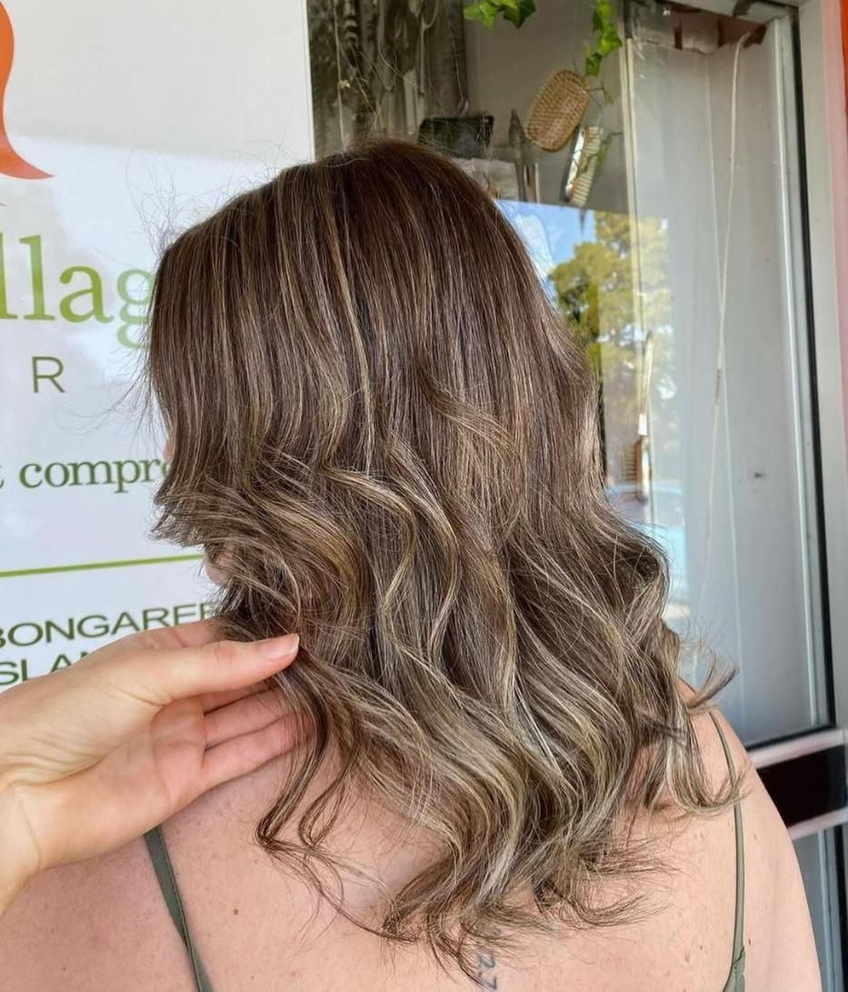 A Woman with Long Brown Hair Is Standing in Front of A Sign — Eco Village Hair in Bongaree, QLD