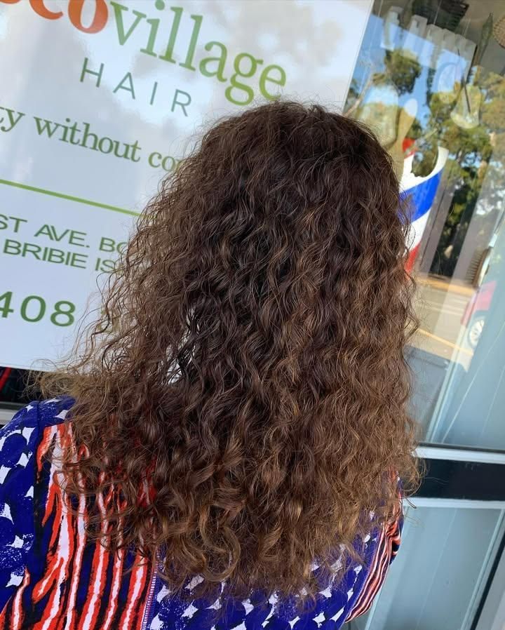 A Woman with Curly Hair Is Wearing an American Flag Shirt — Eco Village Hair in Bongaree, QLD