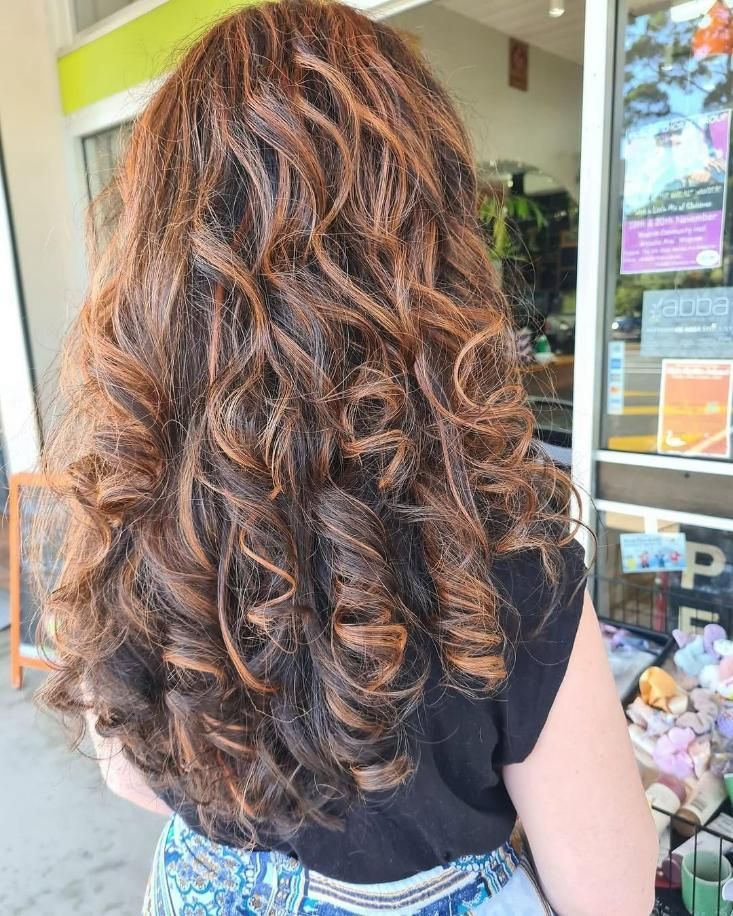 A Woman with Long Curly Hair Is Standing in Front of A Store — Eco Village Hair in Bongaree, QLD