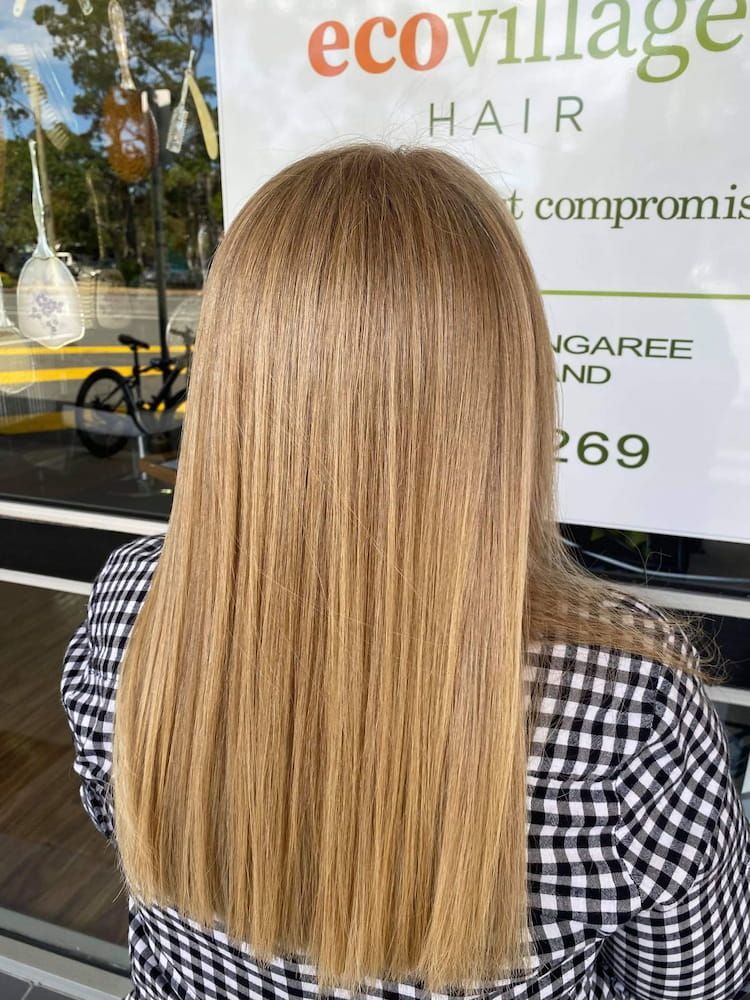 A Woman With Long Blonde Hair is Standing in Front of a Sign That Says Ecovillage Hair — Eco Village Hair in Bongaree, QLD