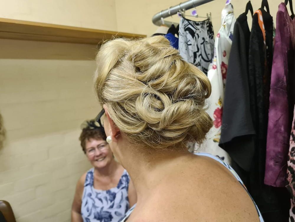 A Woman With Her Hair in a Bun is Looking at Herself in the Mirror — Eco Village Hair in Bongaree, QLD