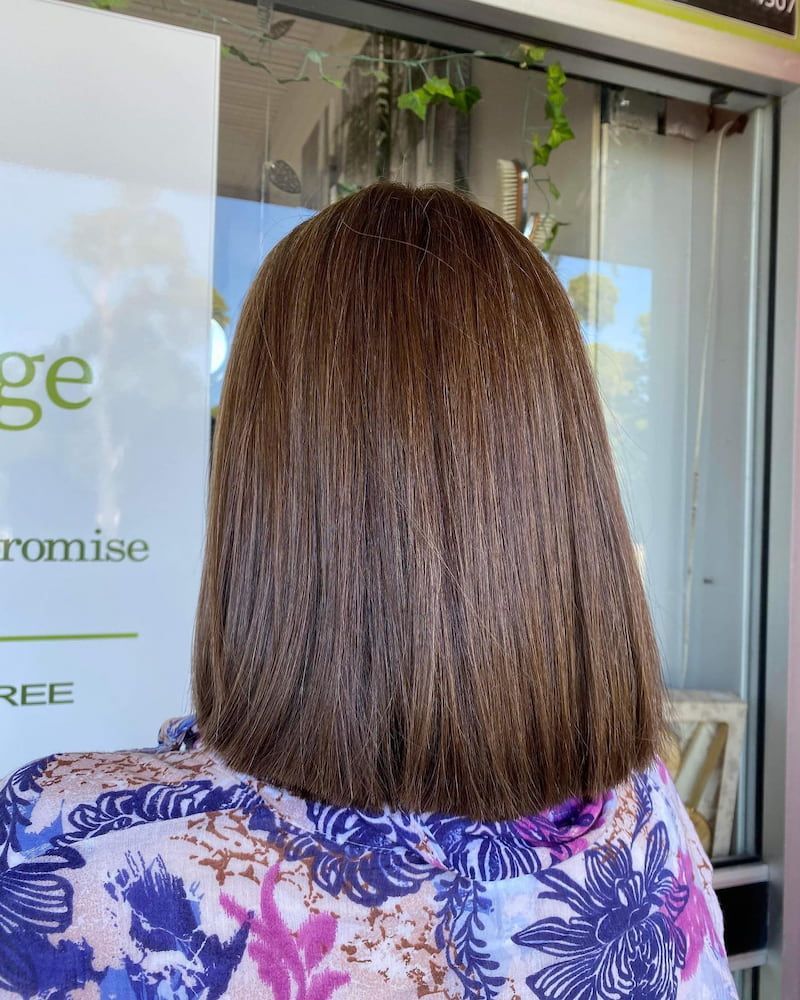 A Woman With Long Brown Hair is Standing in Front of a Window — Eco Village Hair in Bongaree, QLD