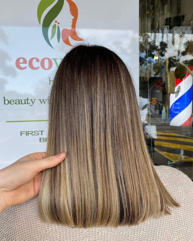 A Person is Holding a Woman's Hair in Front of a Sign That Says Eco — Eco Village Hair in Bongaree, QLD