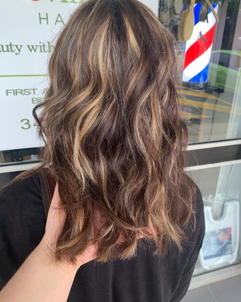 A Woman With Long Brown Hair is Standing in Front of a Barber Shop — Eco Village Hair in Bongaree, QLD