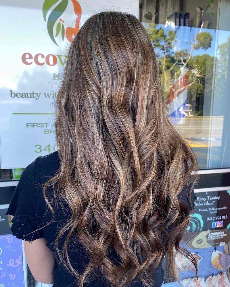 A Woman With Long Brown Hair is Standing in Front of a Window — Eco Village Hair in Bongaree, QLD