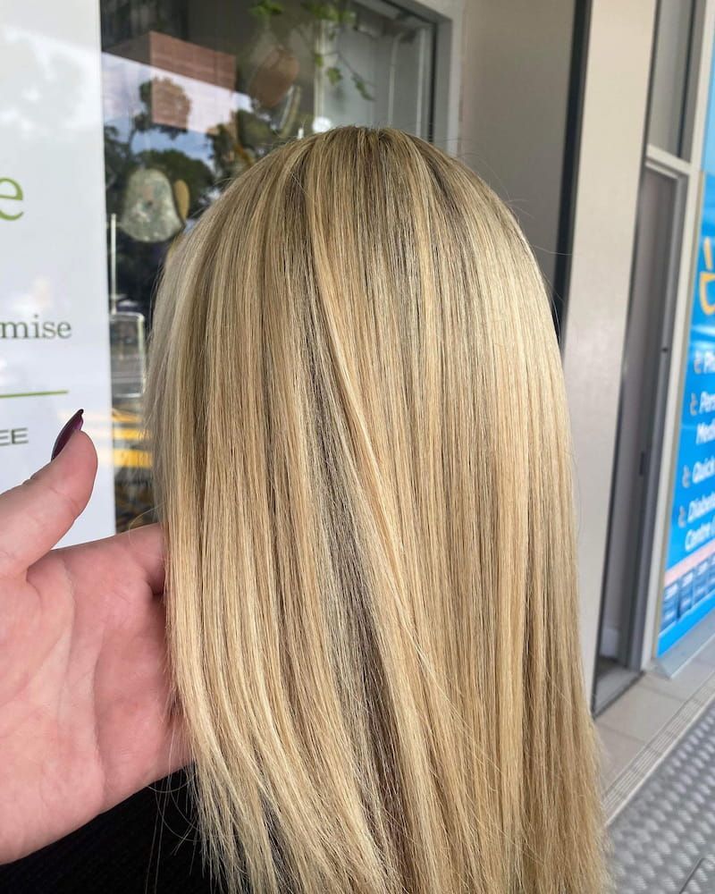A Woman With Long Blonde Hair is Standing in Front of a Window — Eco Village Hair in Bongaree, QLD