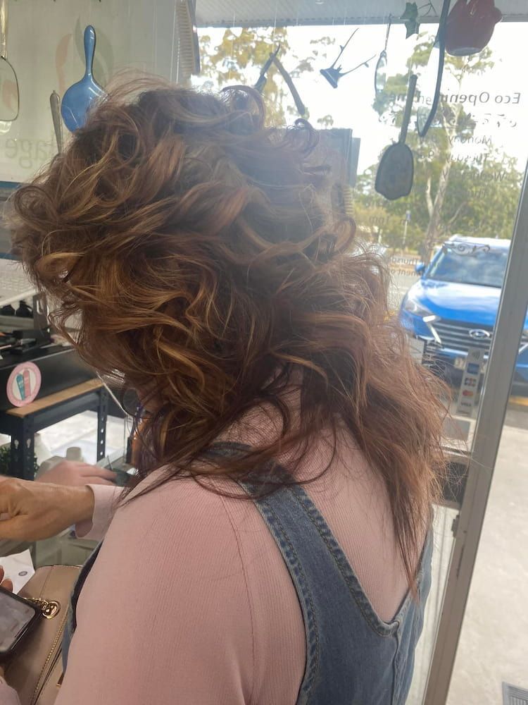 A Woman With Curly Hair is Standing in Front of a Window — Eco Village Hair in Bongaree, QLD