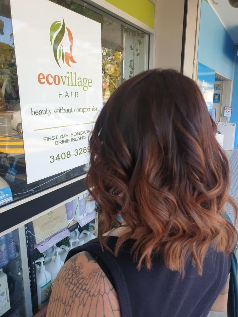 A Woman is Standing in Front of a Window With a Sign That Says Ecovillage Hair — Eco Village Hair in Bongaree, QLD