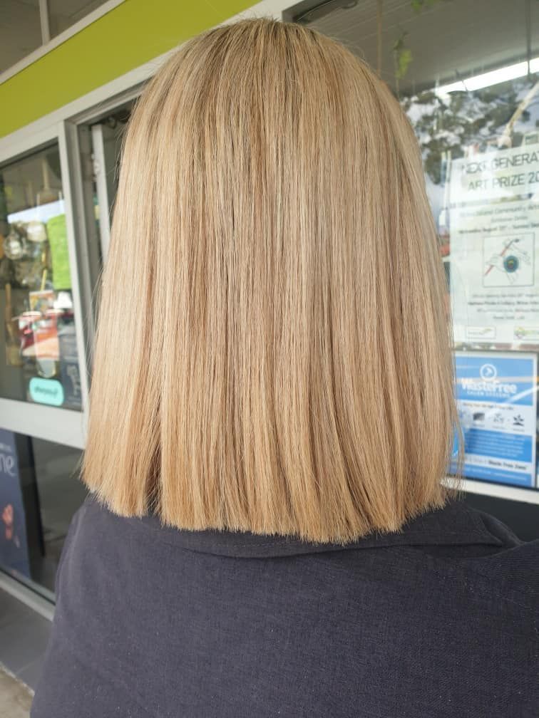 A Woman With Blonde Hair is Standing in Front of a Window — Eco Village Hair in Bongaree, QLD