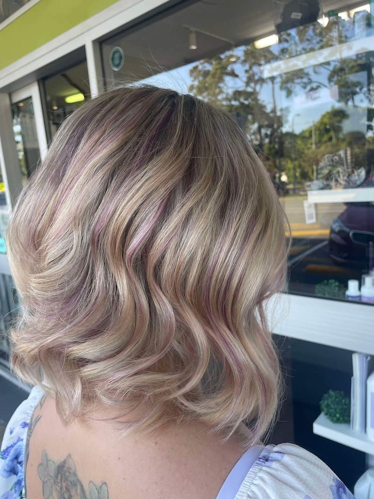 A Woman With Blonde Hair and a Tattoo on Her Back is Standing in Front of a Window — Eco Village Hair in Bongaree, QLD