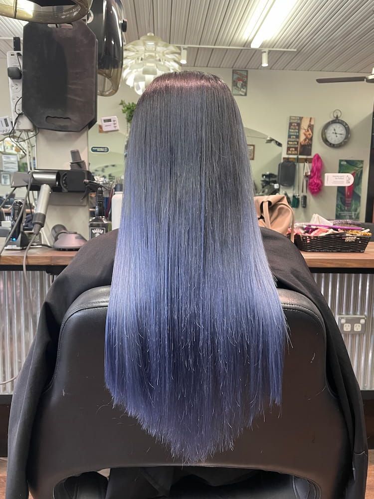 A Woman With Long Blue Hair is Sitting in a Chair in a Salon — Eco Village Hair in Bongaree, QLD