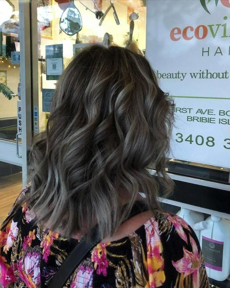 A Woman Is Standing in Front of A Sign that Says Eco Village Hair Salon — Eco Village Hair in Bongaree, QLD