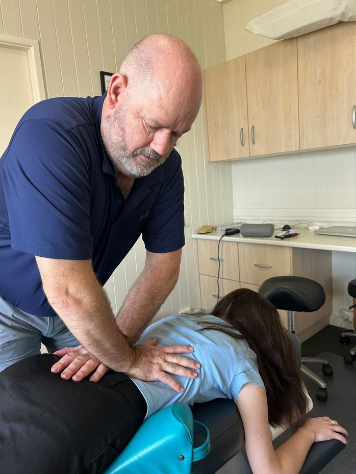 Woman in Blue Shirt Examining Patient's Neck in a Medical Office — Wide Bay Chiropractic in Gympie, QLD