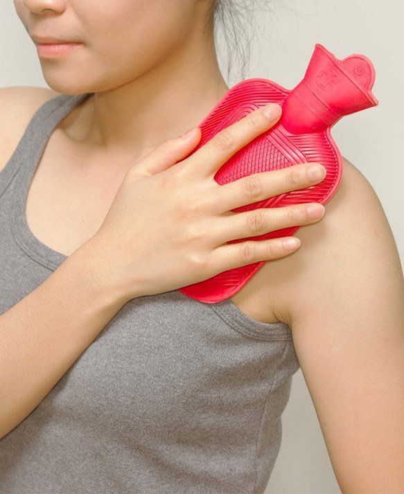 Woman Holding a Red Hot Water Bottle on Her Shoulder — Wide Bay Chiropractic in Gympie, QLD