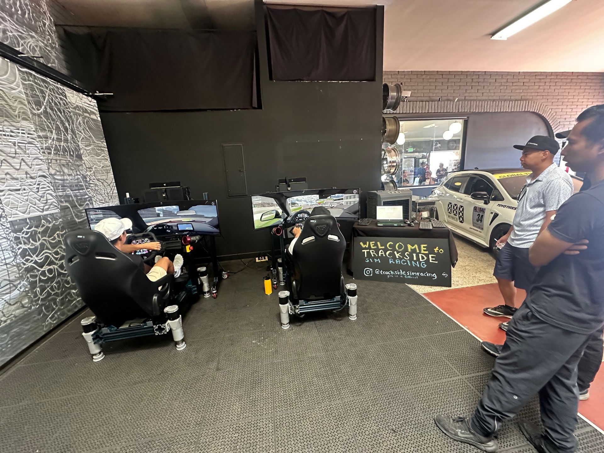 People playing racing video games in a sim racing setup. A car is on display nearby.