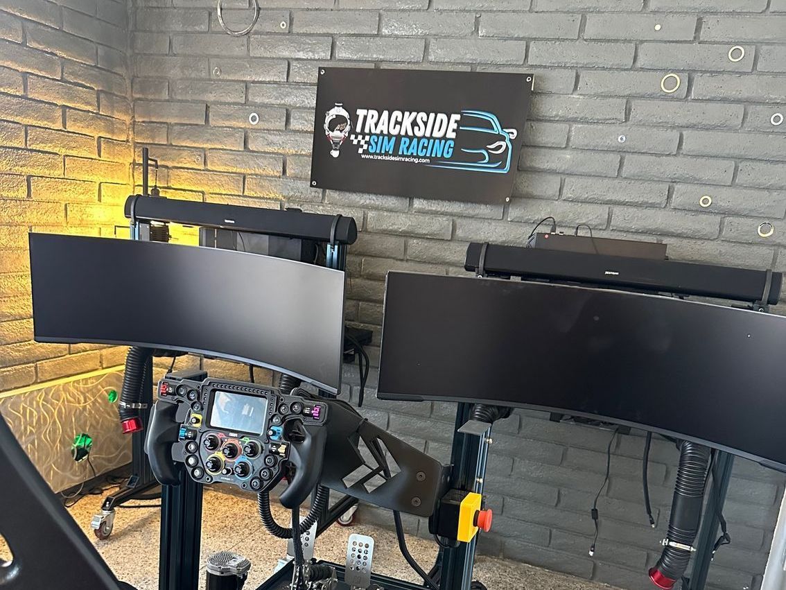Sim racing setup with a steering wheel, monitors, and brick wall background.
