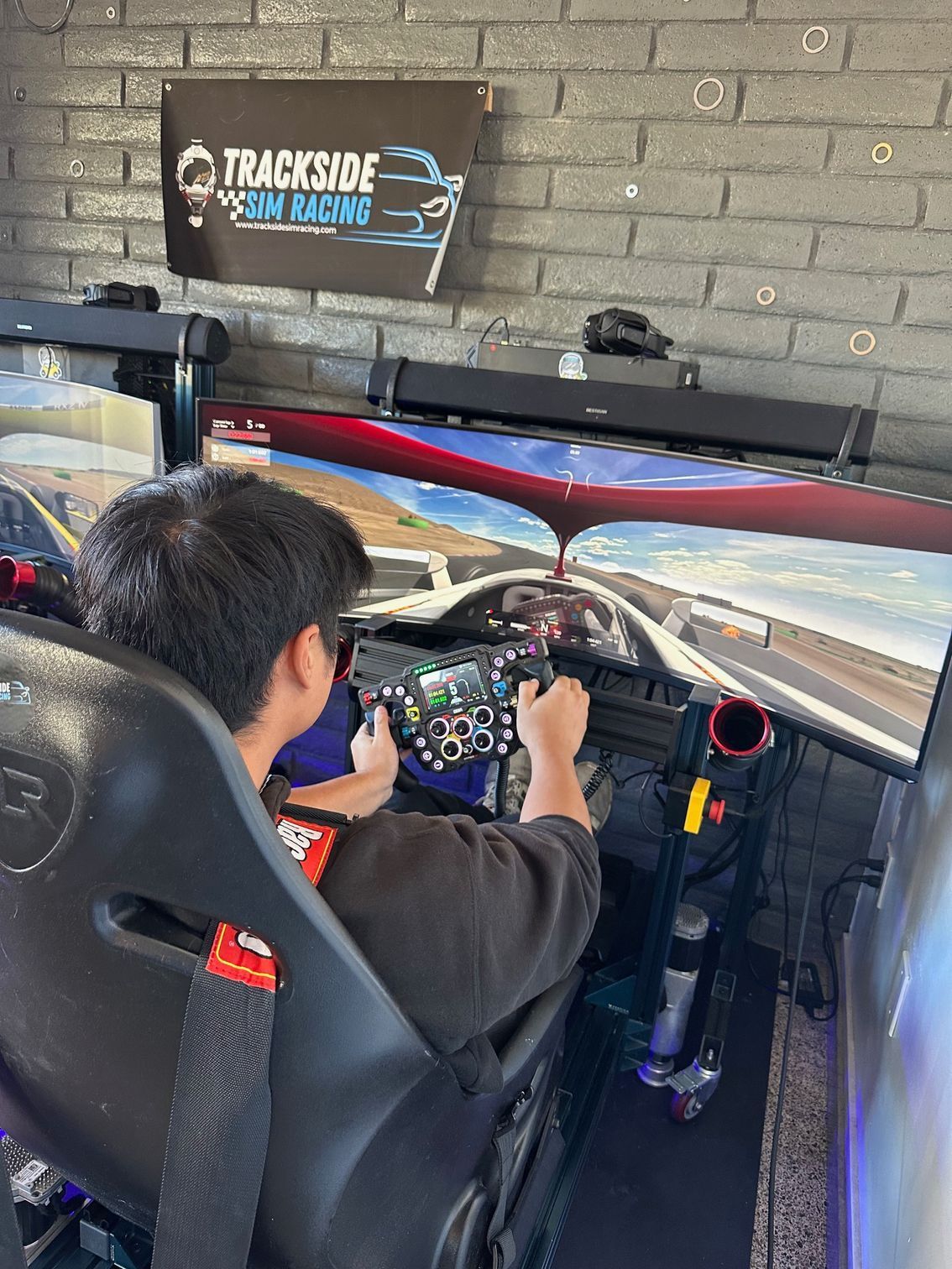Person using a racing simulator with three screens, hands on the steering wheel.