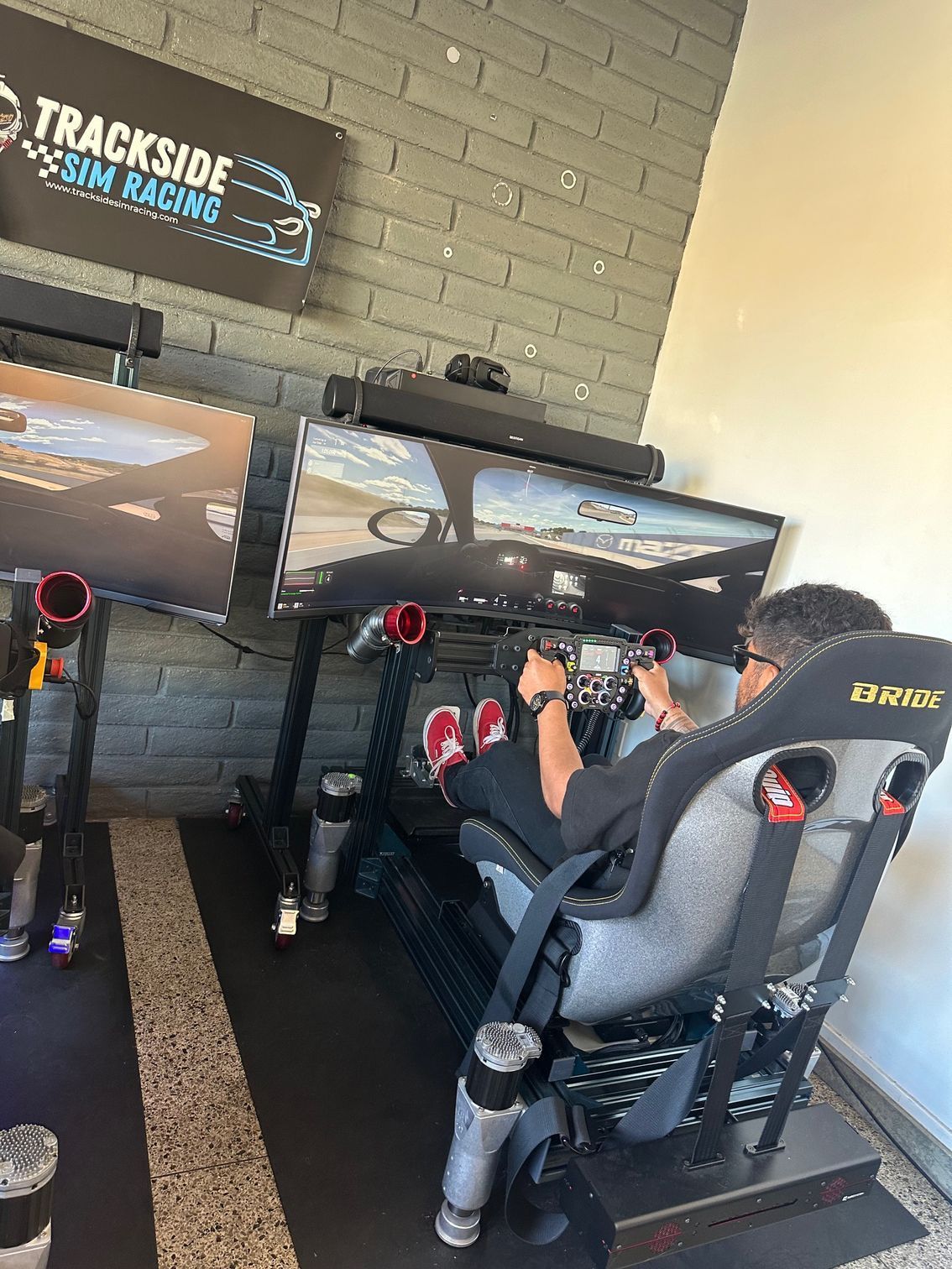 Man racing in a sim setup at Trackside Sim Racing, using a wheel, pedals, and monitors.