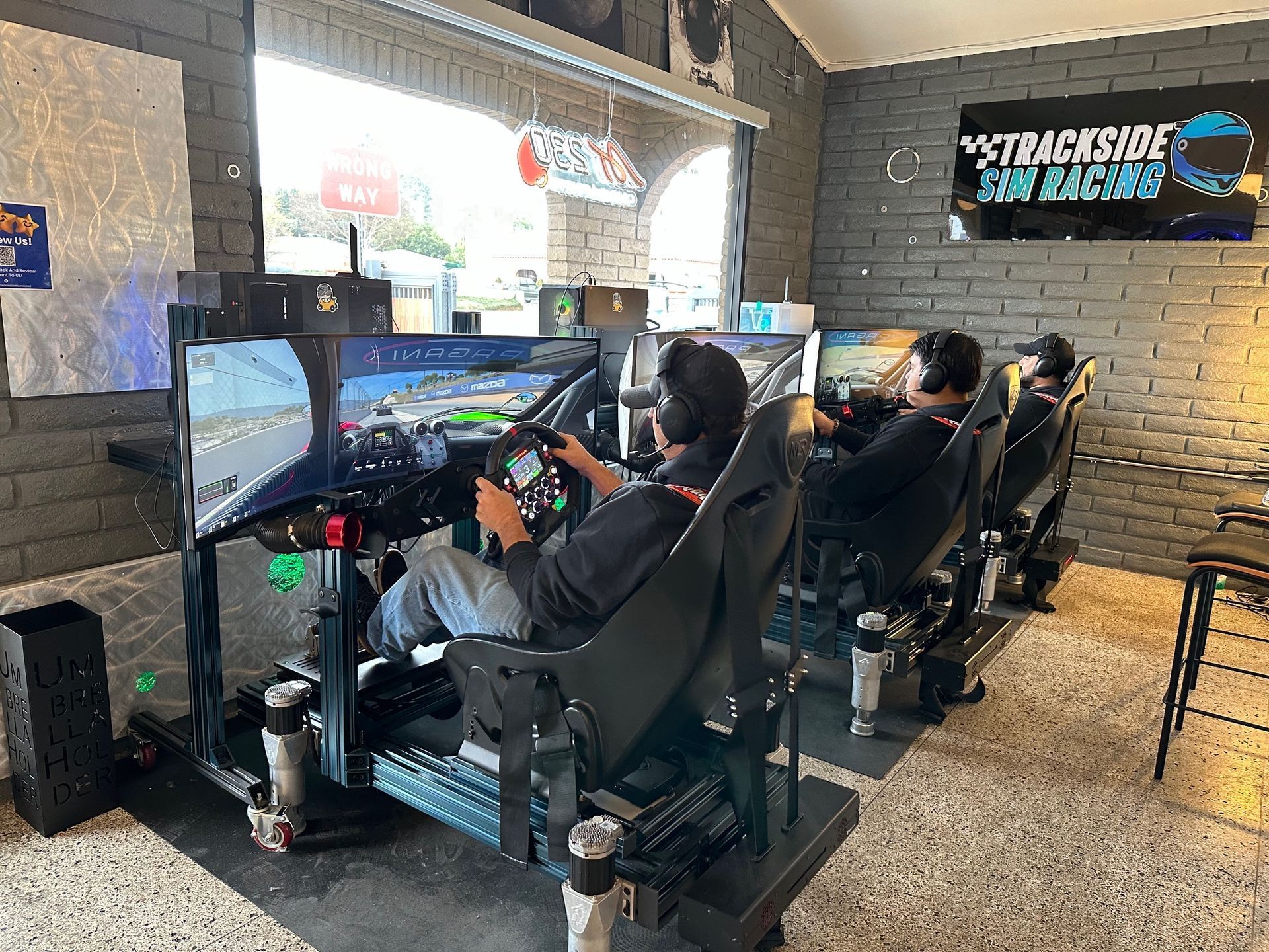Three people racing sim in a room with monitors and racing seats.